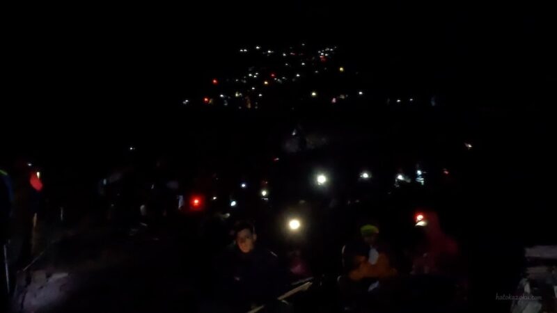 富士登山の夜間登山で、多くの登山者がヘッドライトを点けて行列を作りながら進む様子。暗闇の中に無数のライトが光っている。
