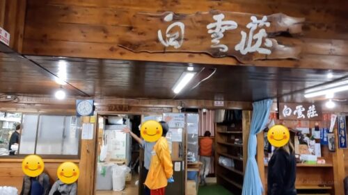 富士登山の山小屋「白雲荘」の館内入口と木製看板の写真。館内で休憩する登山者と温かみのある雰囲気。