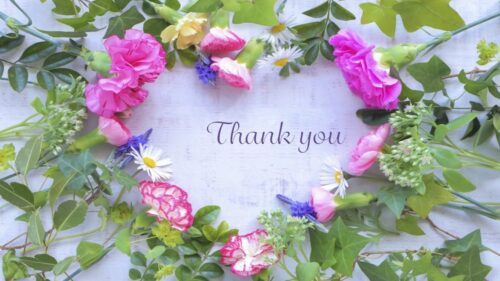 カラフルな花でハート型のリースを作り、中央に「Thank you」と文字が書かれたメッセージカード風の画像。